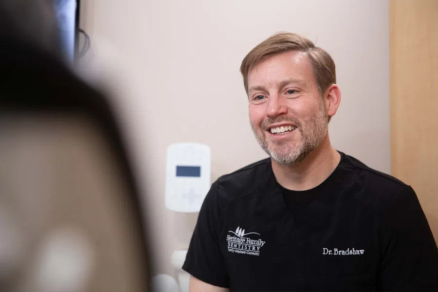 Smiling doctor in a black scrub top engaging with a patient in a medical office setting.