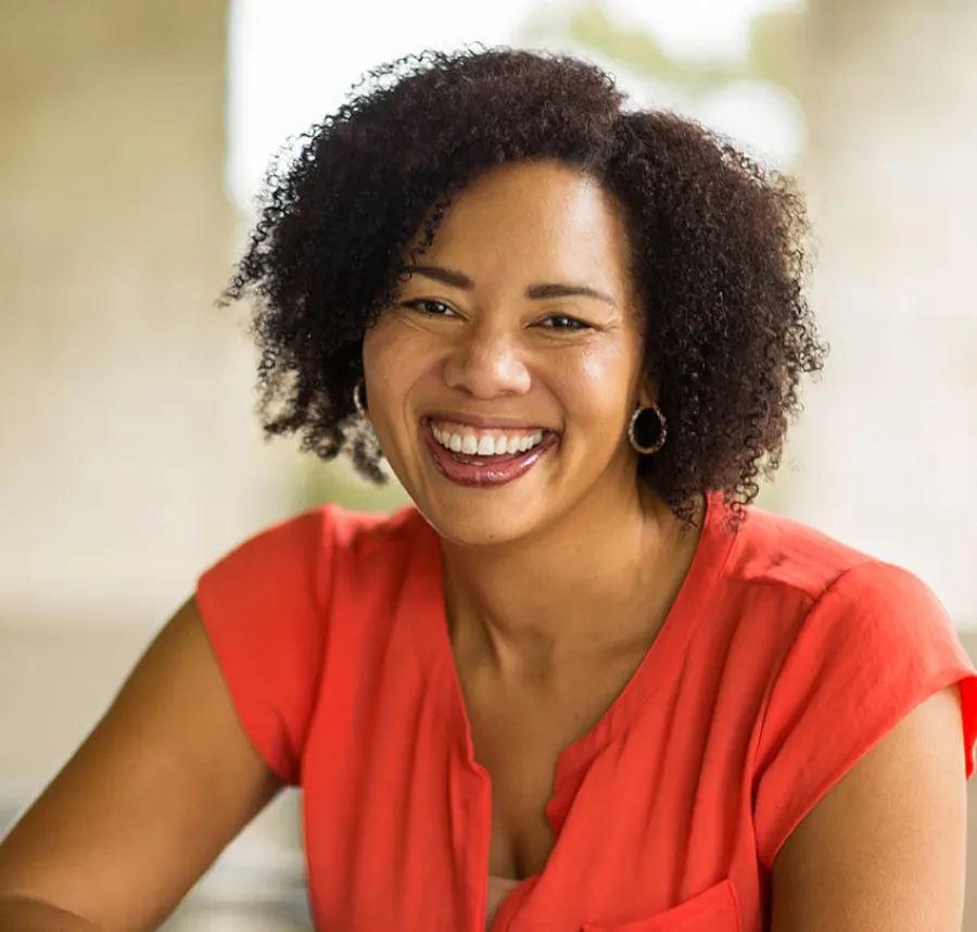 Smiling woman with curly hair wearing a bright red blouse in a softly lit indoor setting