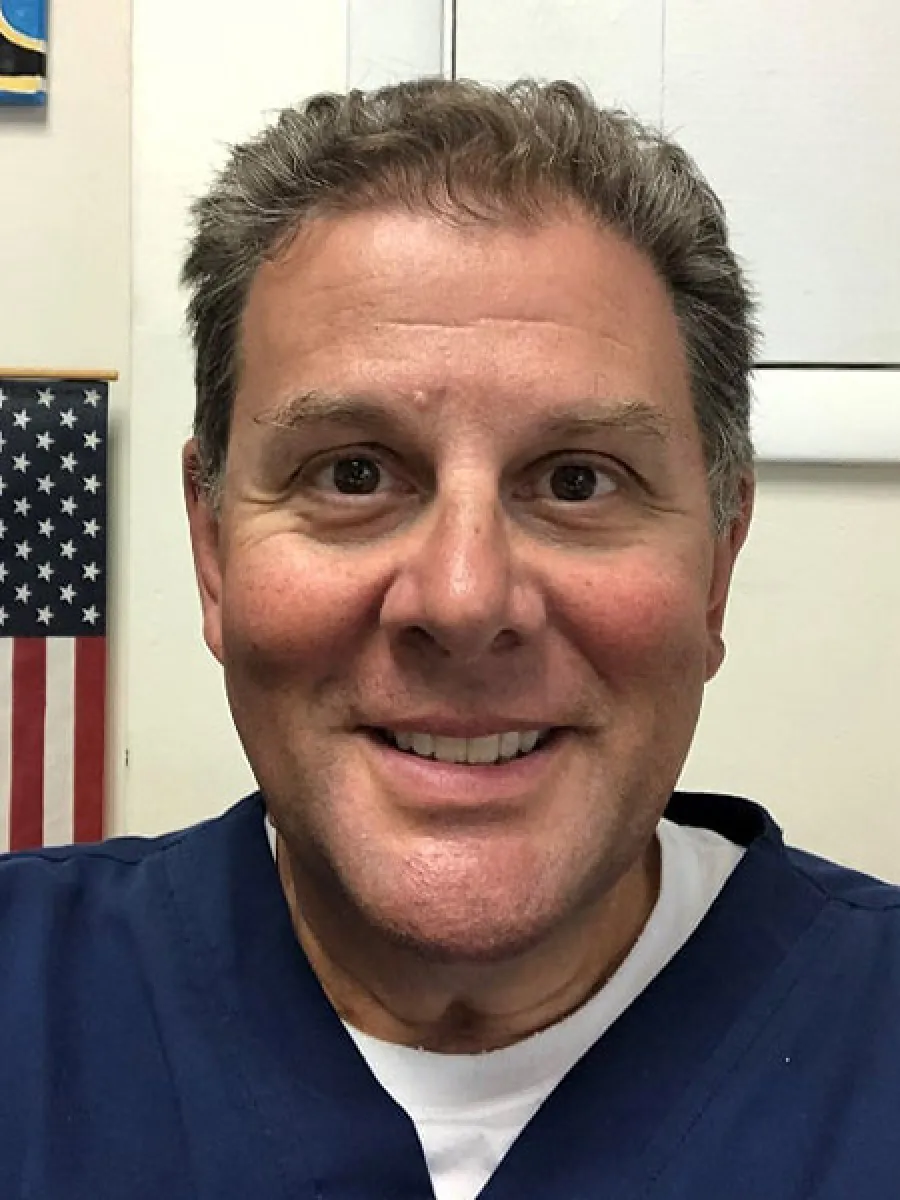 Smiling middle-aged man in navy blue shirt with American flag in background indoors