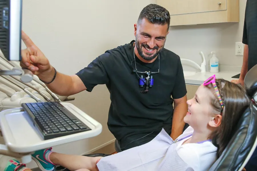 Pediatric dentist smiling and interacting with a child in a dental office setting.