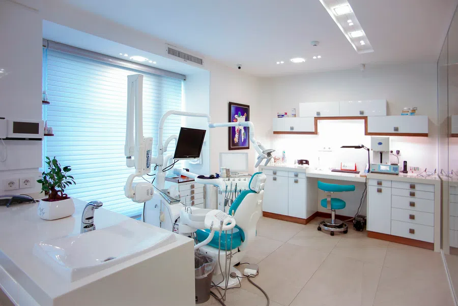 Bright modern dental clinic with dental chair, monitor, sink, and white cabinetry under natural light.