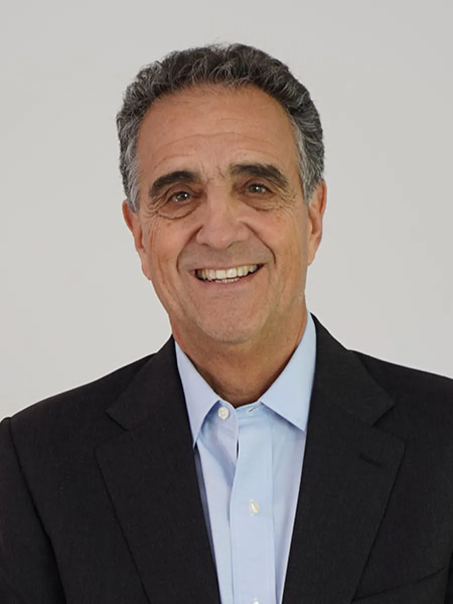 Smiling man in a suit against a plain background, radiating warmth and approachability.