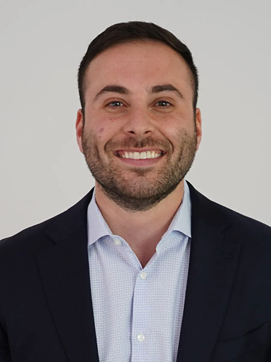 Smiling man in a suit against a neutral background, conveying professionalism and approachability.