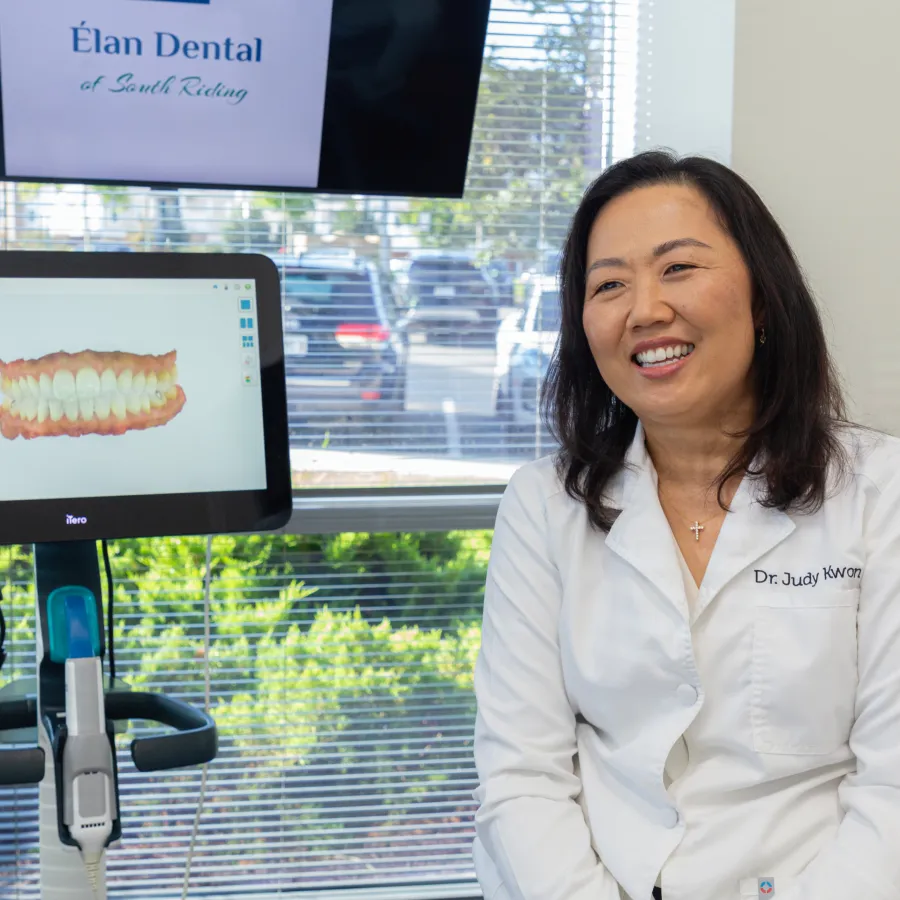 Smiling female dentist Dr. Judy Kwon in white coat at office with dental 3D teeth scan on screen