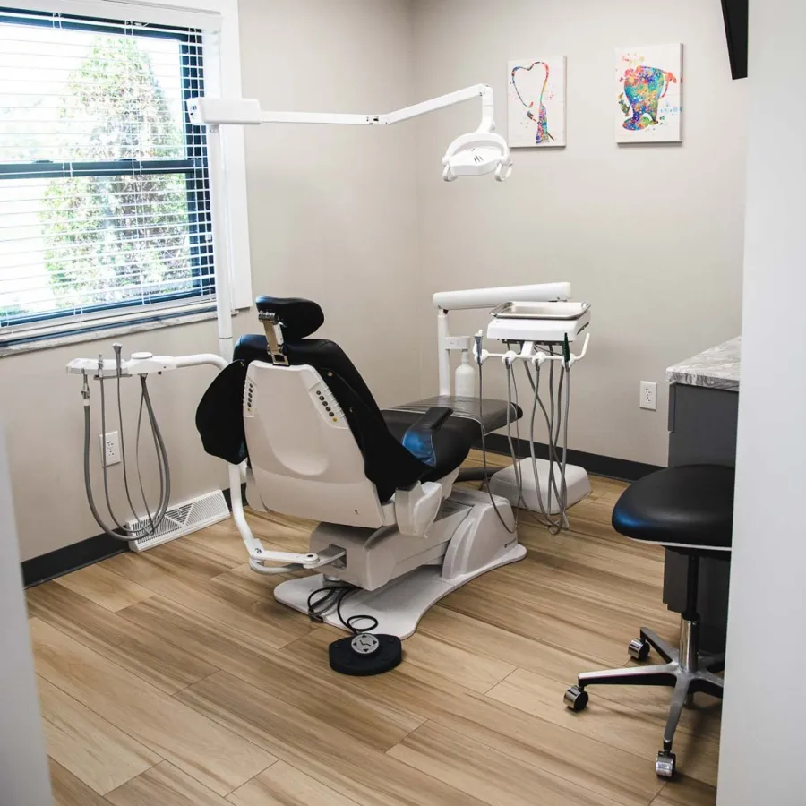 Modern dental office with a patient chair, dental equipment, wooden flooring, and soft wall artworks.