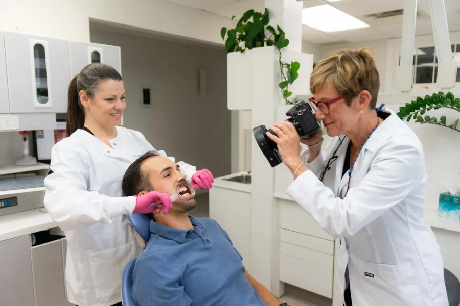 Dentist captures intraoral photos of male patient while dental assistant prepares for examination in clinic