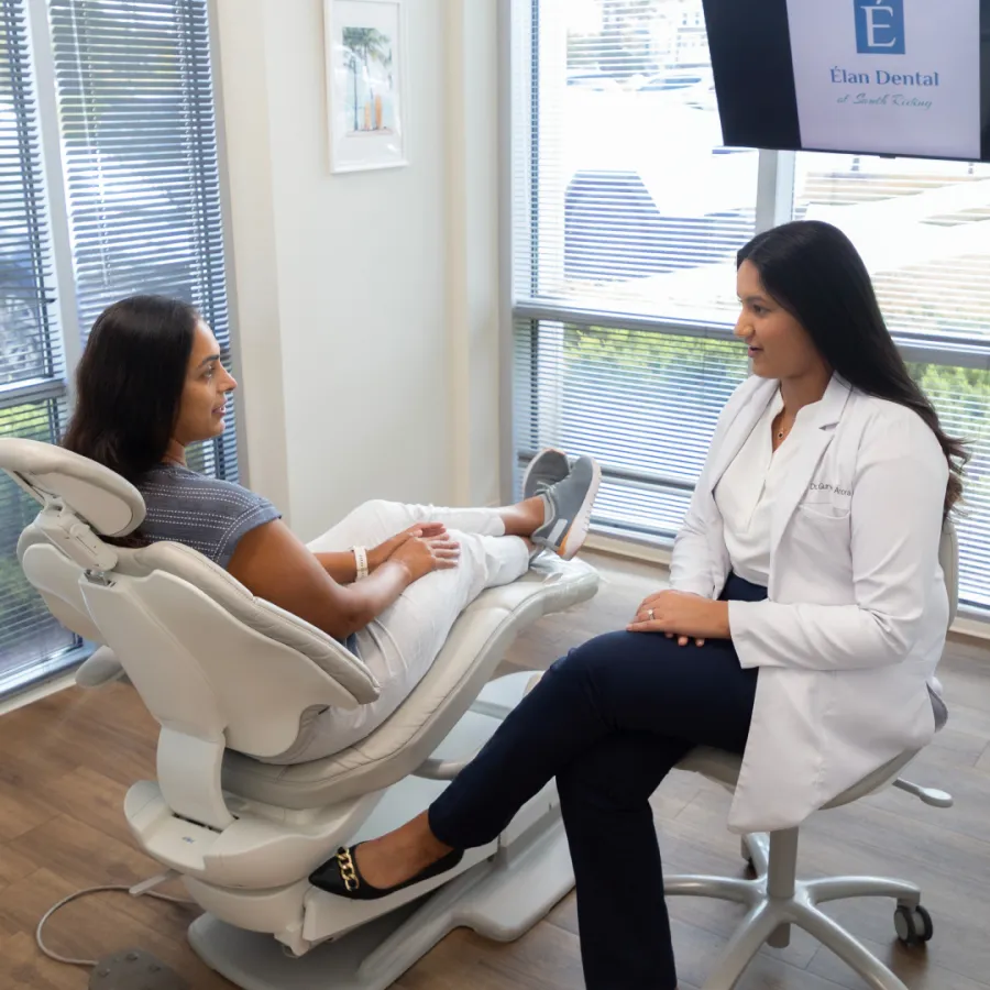 Dental patient consults with female dentist in white coat in a bright modern office with large windows.