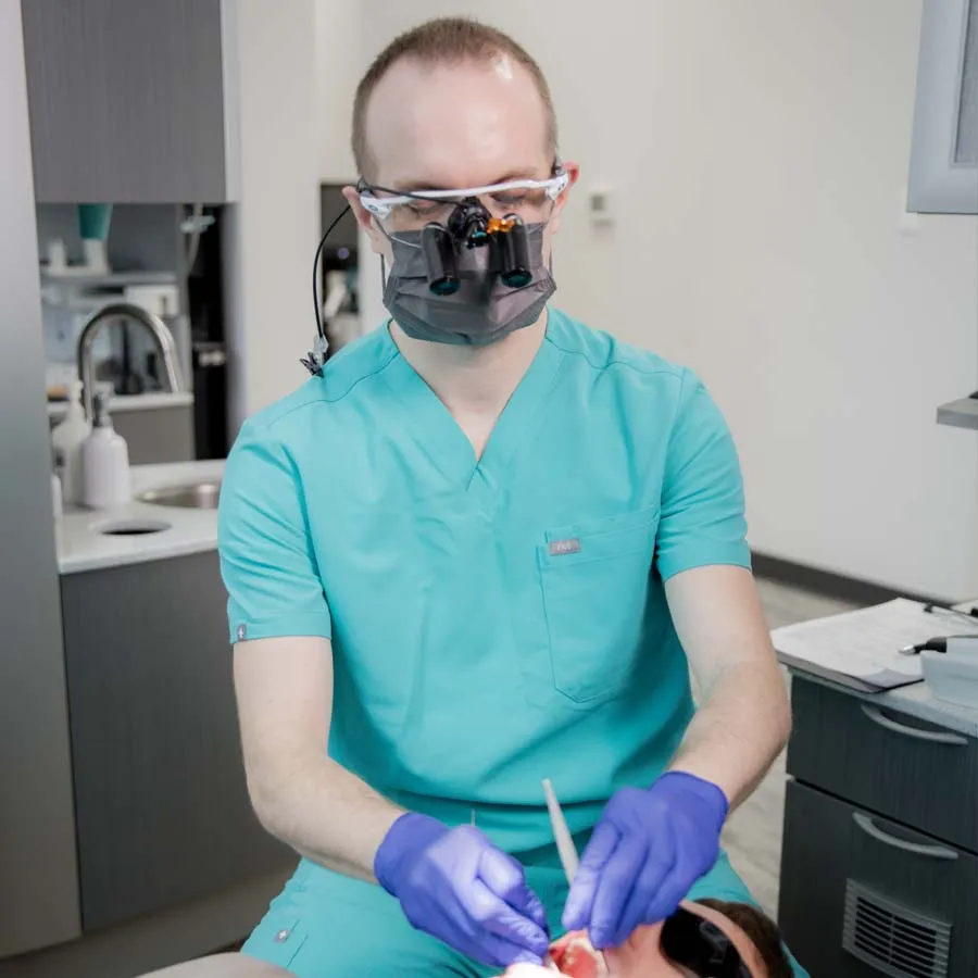 Dentist consulting with elderly male patient reclining in dental chair overlooking snowy outdoor scene.