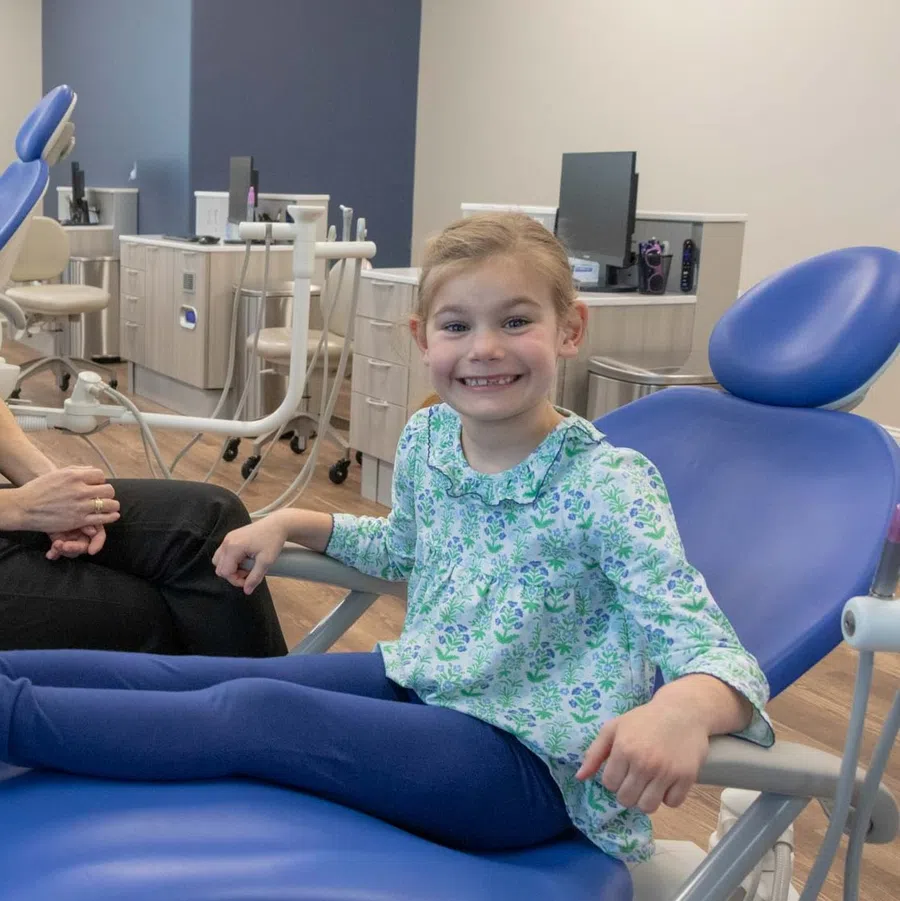 Smiling young girl sitting on dental chair with female dentist in modern clinic room