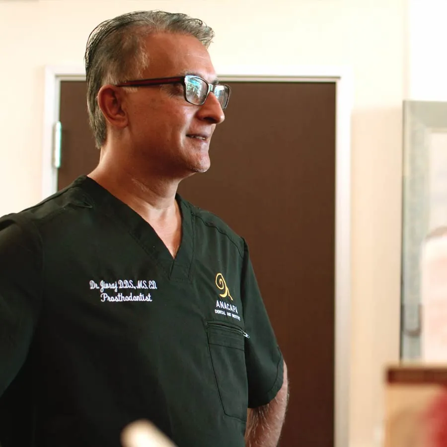 A prosthodontist in scrubs, standing confidently in a dental office environment.