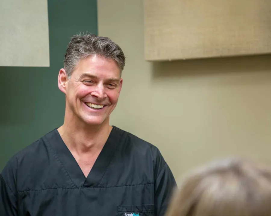 Smiling male healthcare professional in black scrubs interacting with a patient in a clinical setting