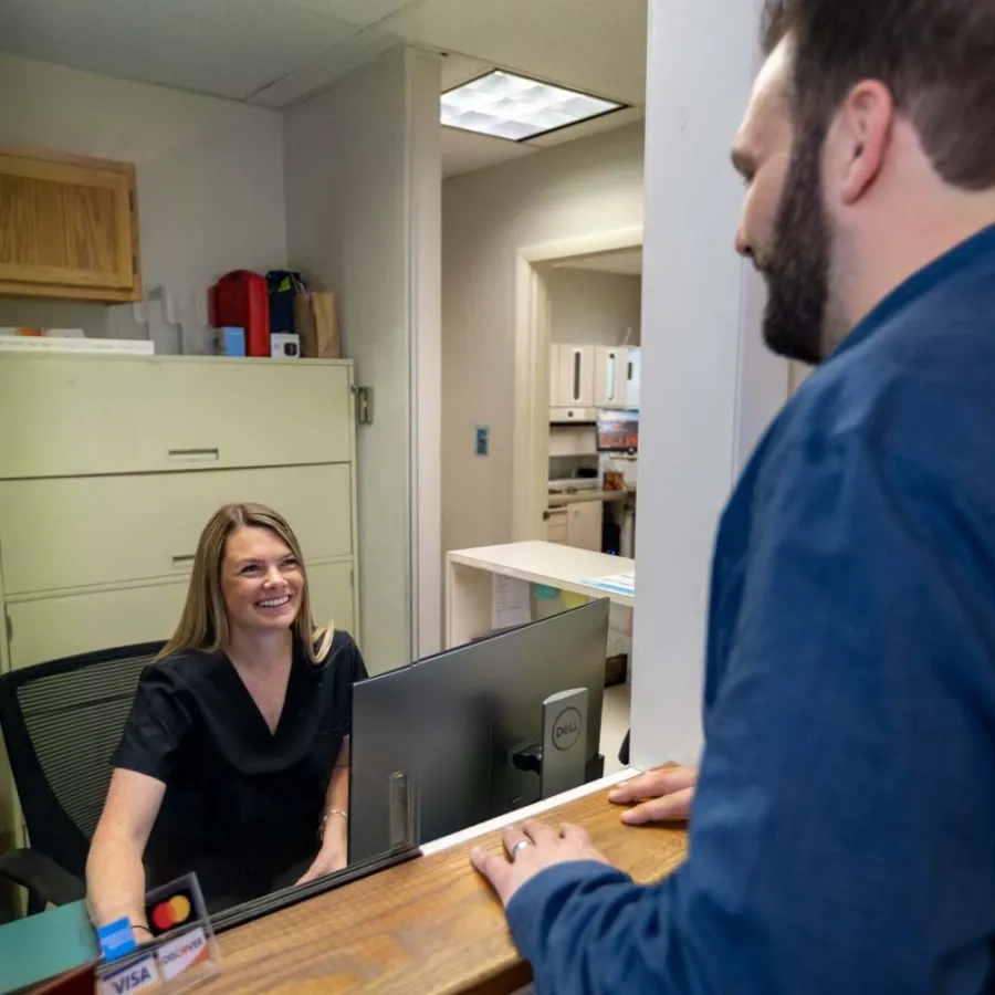 Smiling receptionist in black scrubs attending to male visitor at medical office front desk