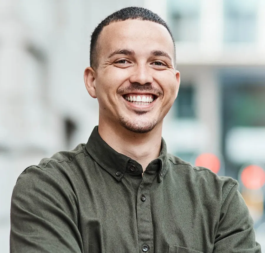 Smiling man in a green shirt standing confidently outdoors with a blurred background.