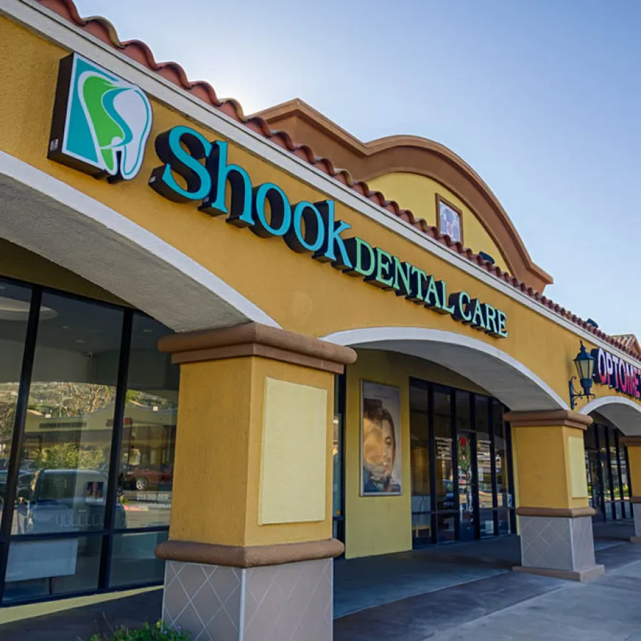 Exterior view of Shook Dental Care clinic with a large tooth logo on yellow building under clear sky