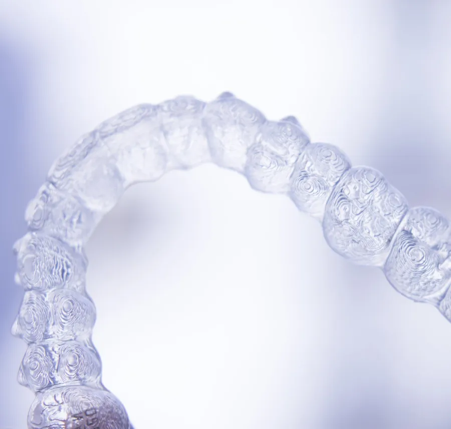 Close-up of a clear dental aligner with detailed tooth impressions on a soft blue background.