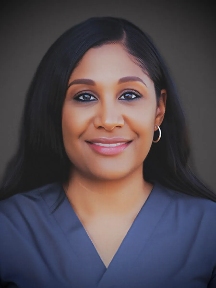 Smiling woman with long dark hair wearing hoop earrings and a blue V-neck top against a dark background