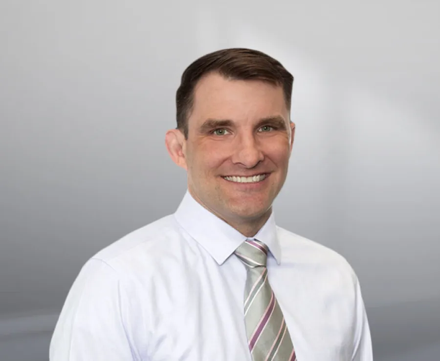 Smiling man in white shirt and striped tie against a simple gray background, professional headshot.