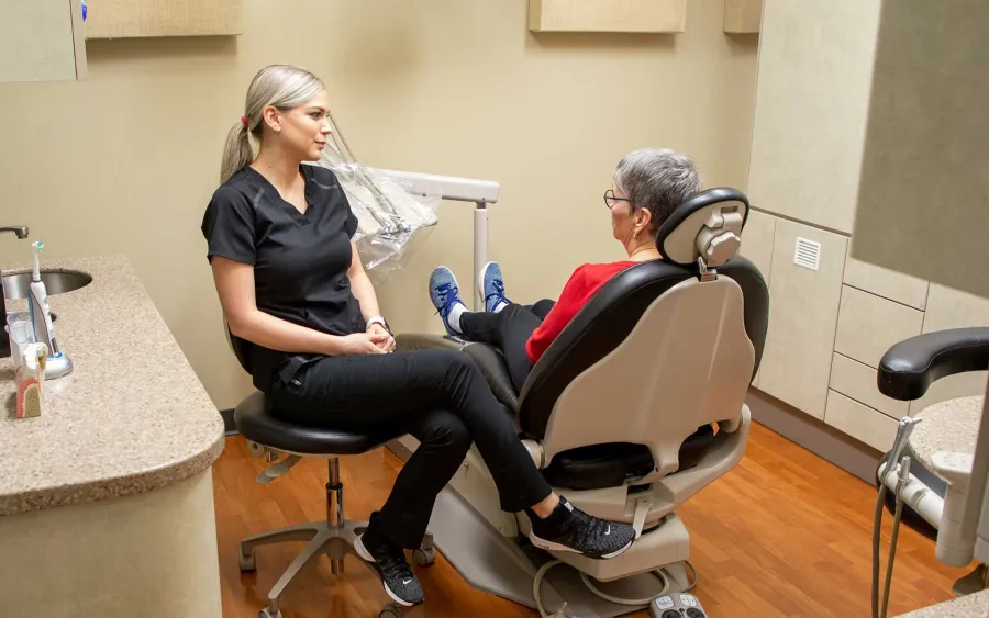 Dentist in black scrubs consulting with elderly patient seated in dental chair in clinic room