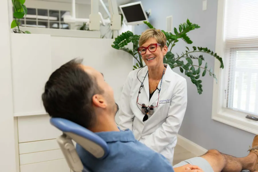 Dentist smiling and talking to male patient reclining in dental chair in bright modern clinic.