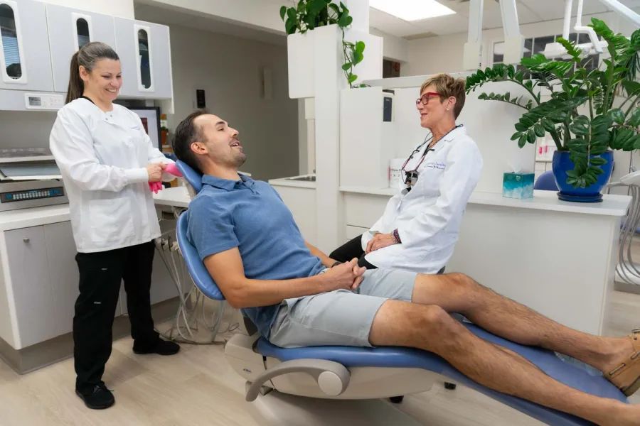Male patient sitting on dental chair smiling with dentist and assistant in a modern clinic setting