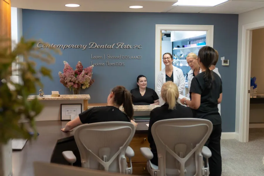 Dental clinic staff in scrubs and white coats chatting in a modern reception area with Contemporary Dental Arts sign.