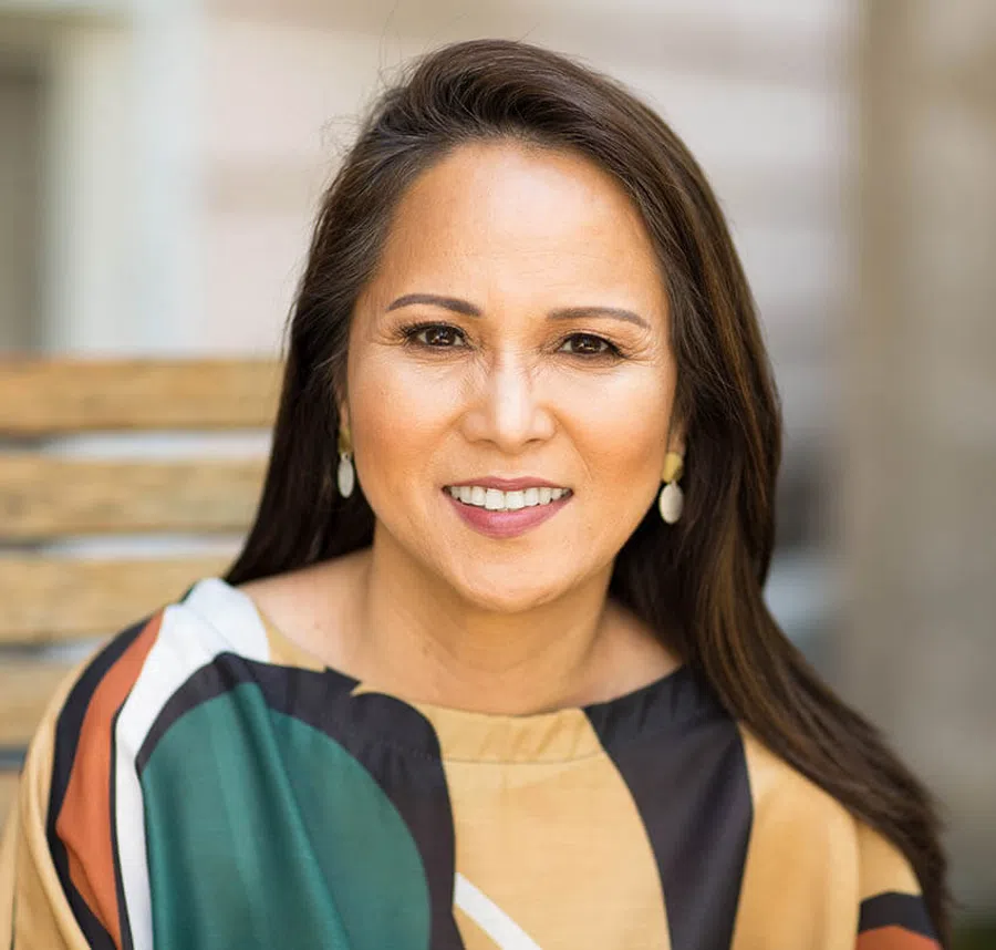 Portrait of a middle-aged woman with long dark hair and colorful blouse smiling outdoors