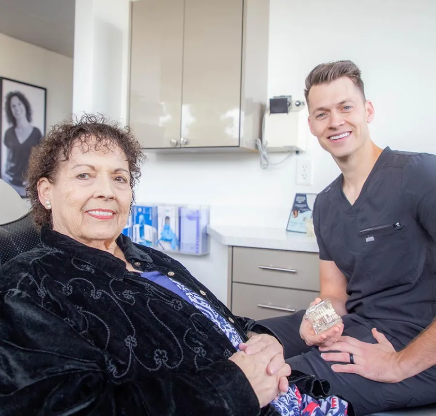 Senior woman smiling with a male dentist holding a dental model in a modern clinic setting.