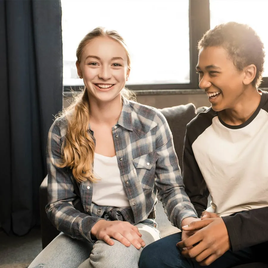 Smiling teenage girl and boy sitting on sofa holding hands and enjoying each other's company indoors