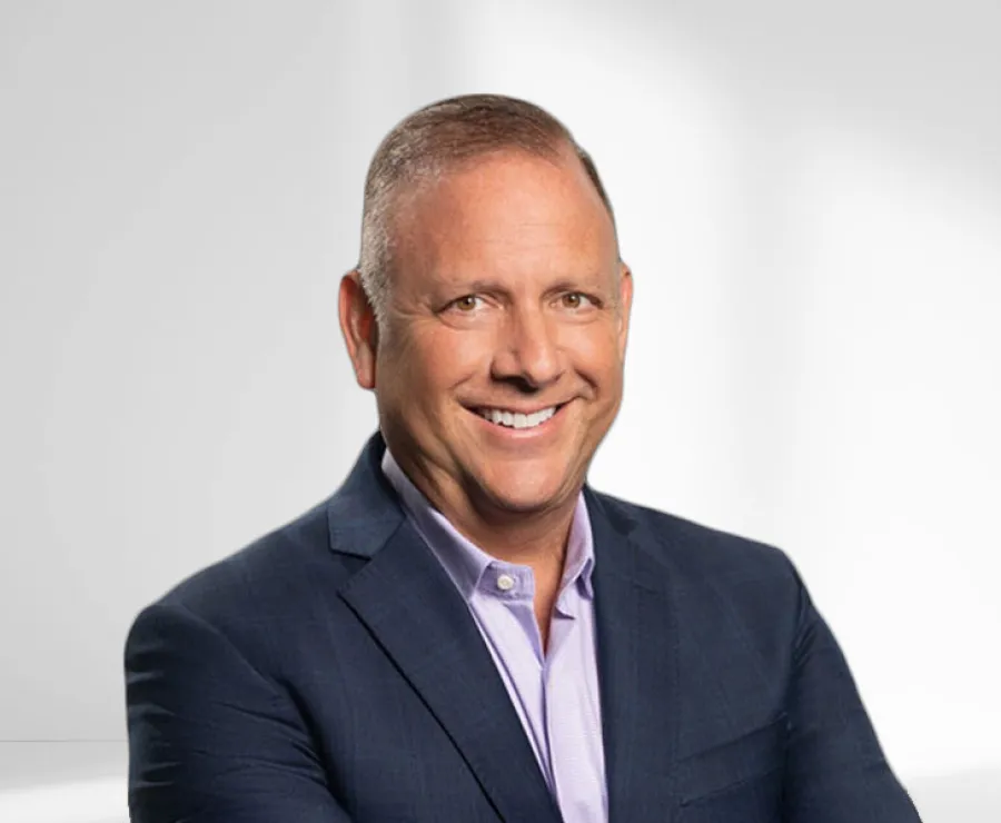 Smiling middle-aged man in a dark blue suit jacket with a light purple shirt on a white background.