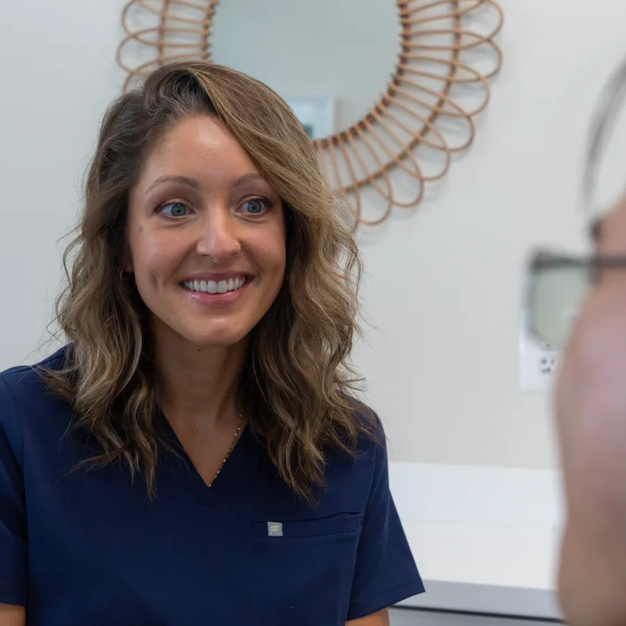 Smiling female healthcare professional in navy scrubs engaging with a patient in a medical office.