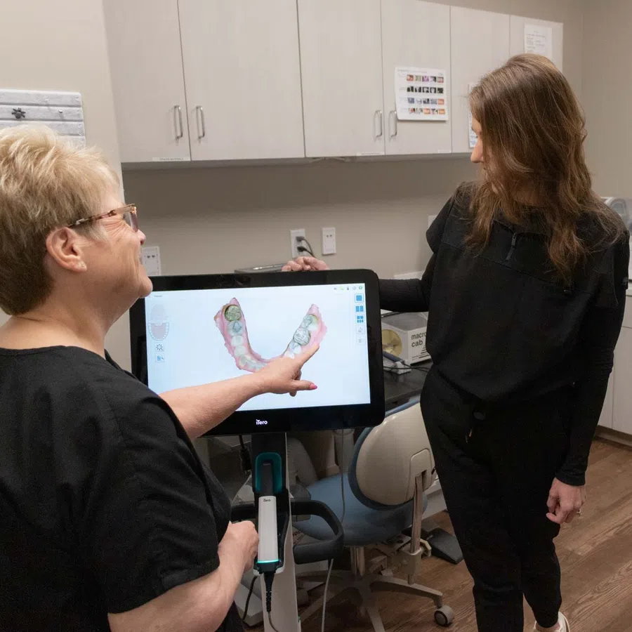 Dental professionals discussing 3D digital dental mold displayed on a screen in clinic office.