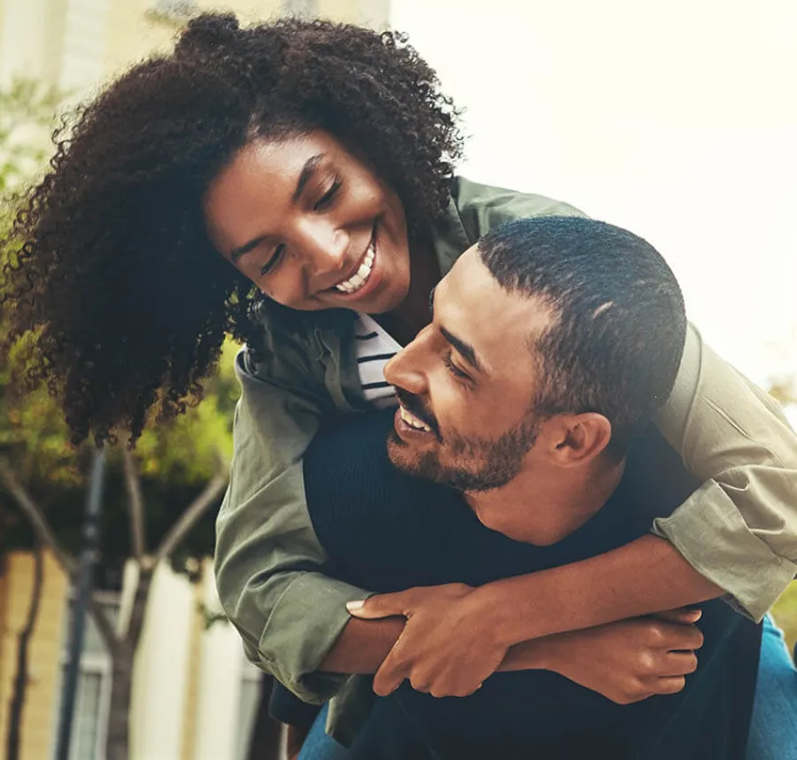 Smiling woman with curly hair hugs man from behind outdoors in a warm, joyful moment