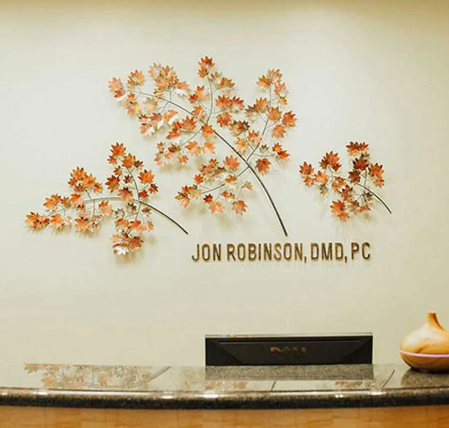 Dentist office reception with autumn leaf wall art and Jon Robinson DMD PC name on beige wall.