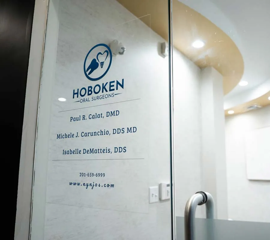 Glass door of Hoboken Oral Surgeons office listing three dentists and contact information.