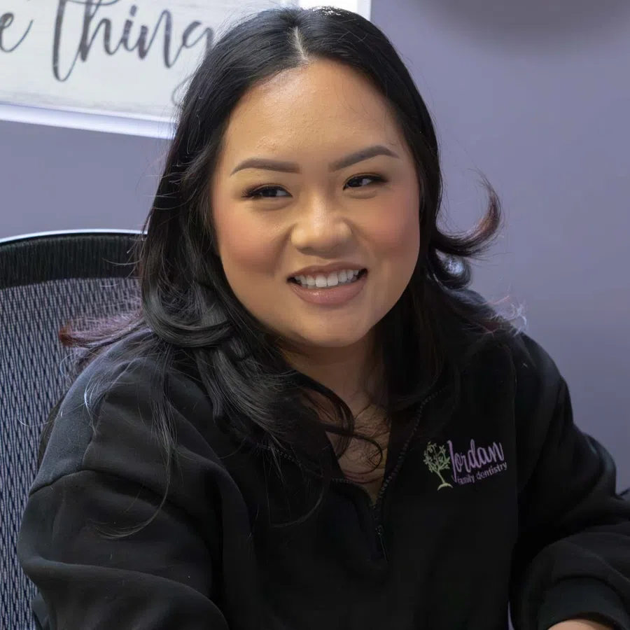 Smiling woman in black jacket engages in conversation in a cozy office setting with light purple walls.