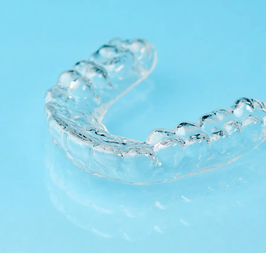 Clear transparent dental aligner for teeth straightening on a light blue background with reflection.