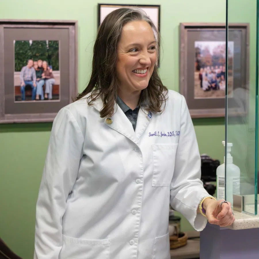 Female doctor in white coat smiling and interacting with patients in a medical office reception area.