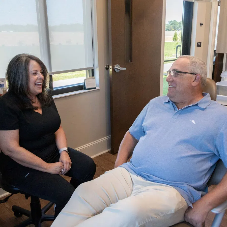 Dentist and male patient smiling and talking during a dental checkup in a modern clinic room.