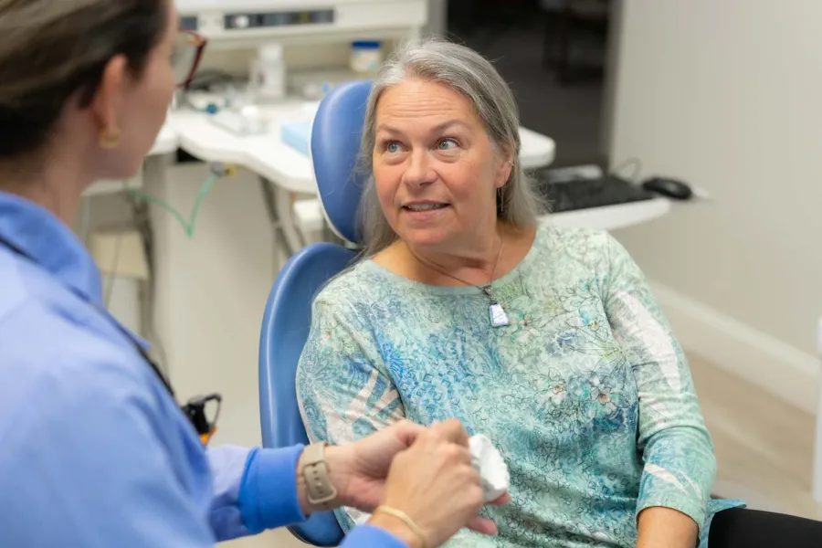 Mature woman in dental chair consulting with dentist about dental mold in clinic setting.