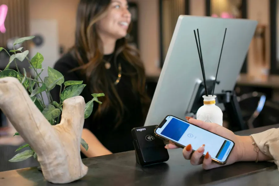 Customer using mobile phone for contactless payment at a salon reception counter with a smiling staff member.