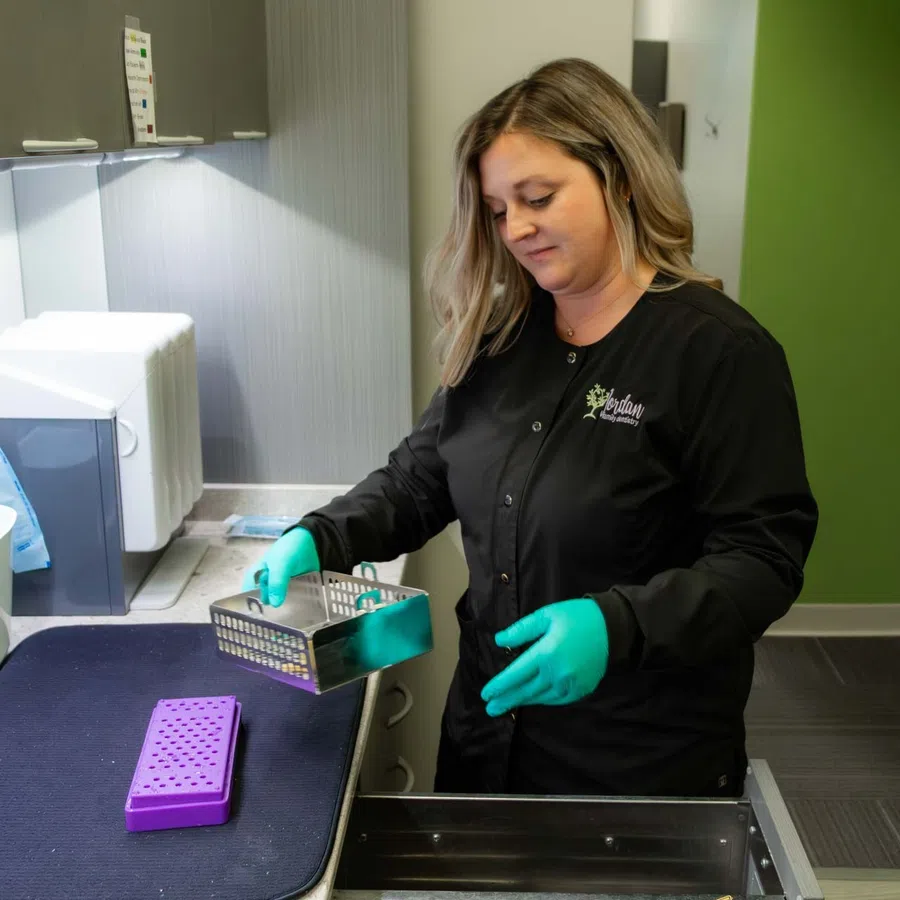 Lab technician wearing gloves handling metal container in a clean laboratory with green and white walls.