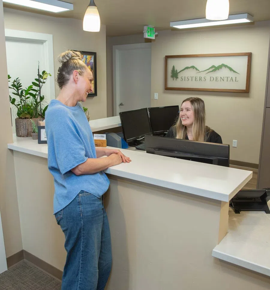Patient speaking with receptionist at Sisters Dental office reception desk with logo and computers.