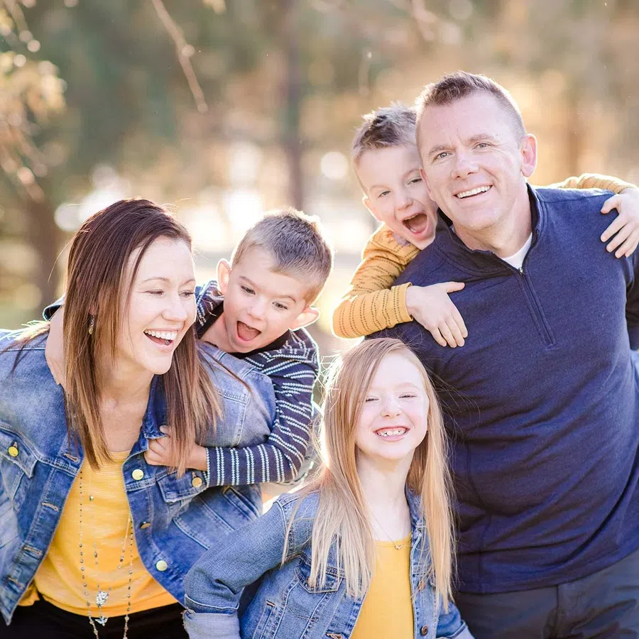 Happy family of five outdoors with parents giving piggyback rides to their children on a sunny day