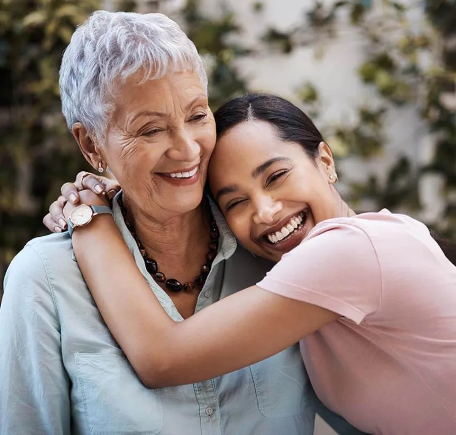 Smiling young woman hugging happy elderly woman outdoors showing love and affection between generations.