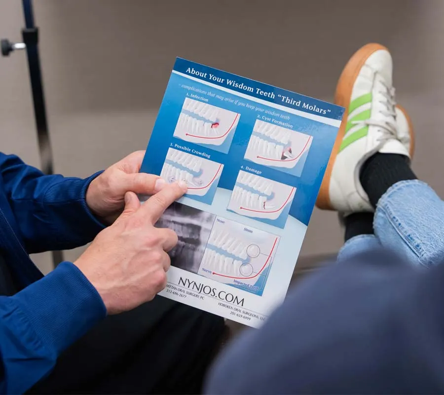 Person pointing to a dental brochure explaining wisdom teeth issues and treatments with images and diagrams.