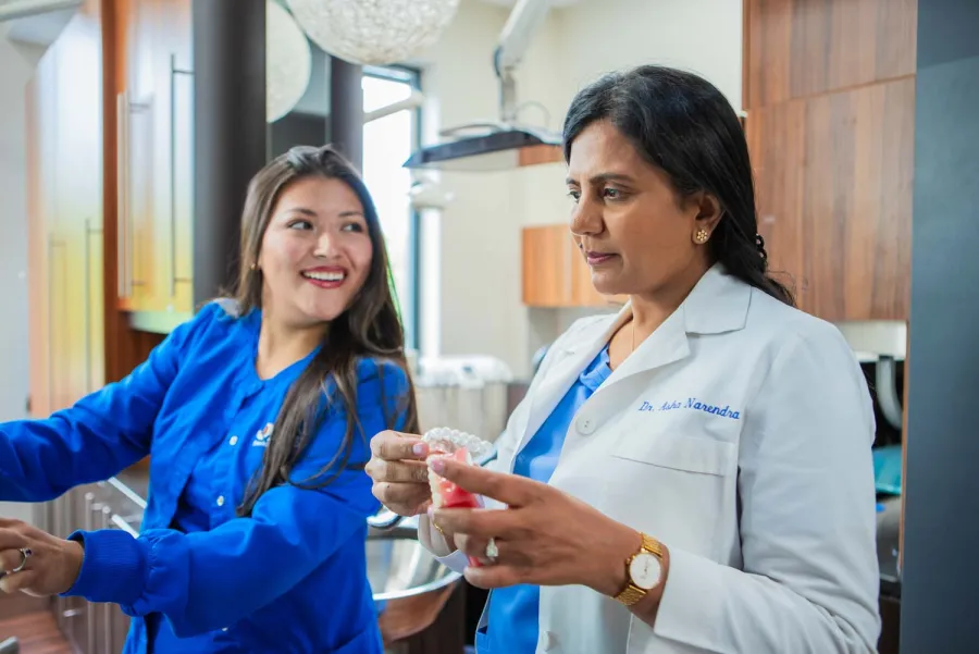 Female dentist explains dental mold to smiling assistant in modern dental office setting.