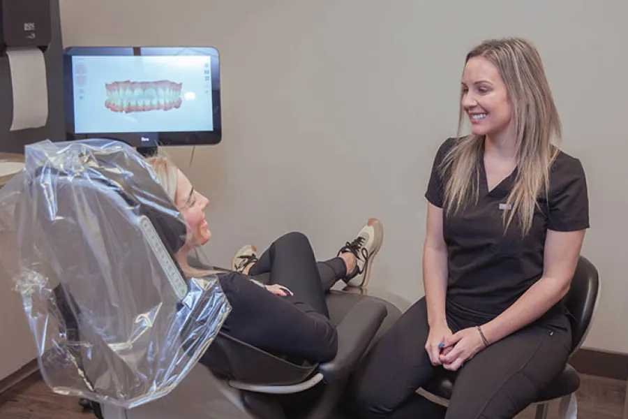 Dentist smiling and consulting with patient reclining in dental chair with dental image on monitor