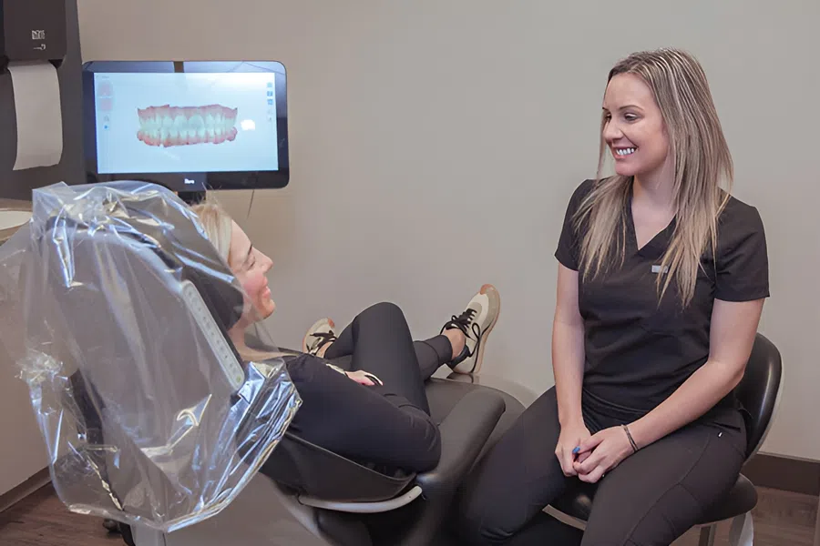 Dentist and patient discussing 3D dental scan in modern clinic with computer screen showing teeth model.