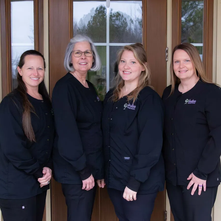 Four women in black uniforms standing in front of a wooden door with glass panes, smiling at the camera.
