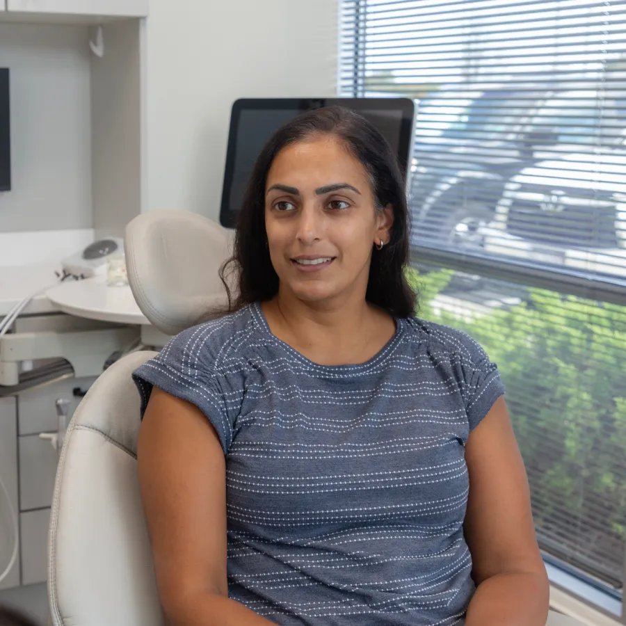 Woman sitting in a dental chair smiling with a dental office and window blinds in the background